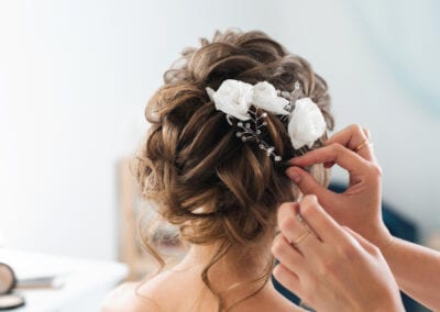 A professional hairstylist gracefully adorns the bride's hair with delicate flowers, adding a touch of natural beauty to her appearance. Best salon in baton rouge.