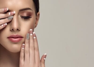 A stunning woman with flawless white nails and makeup showcases a pale-pink French manicure adorned with a rhinestone done by a professional nail technicians. She exudes elegance and style. Best salon in baton rouge.